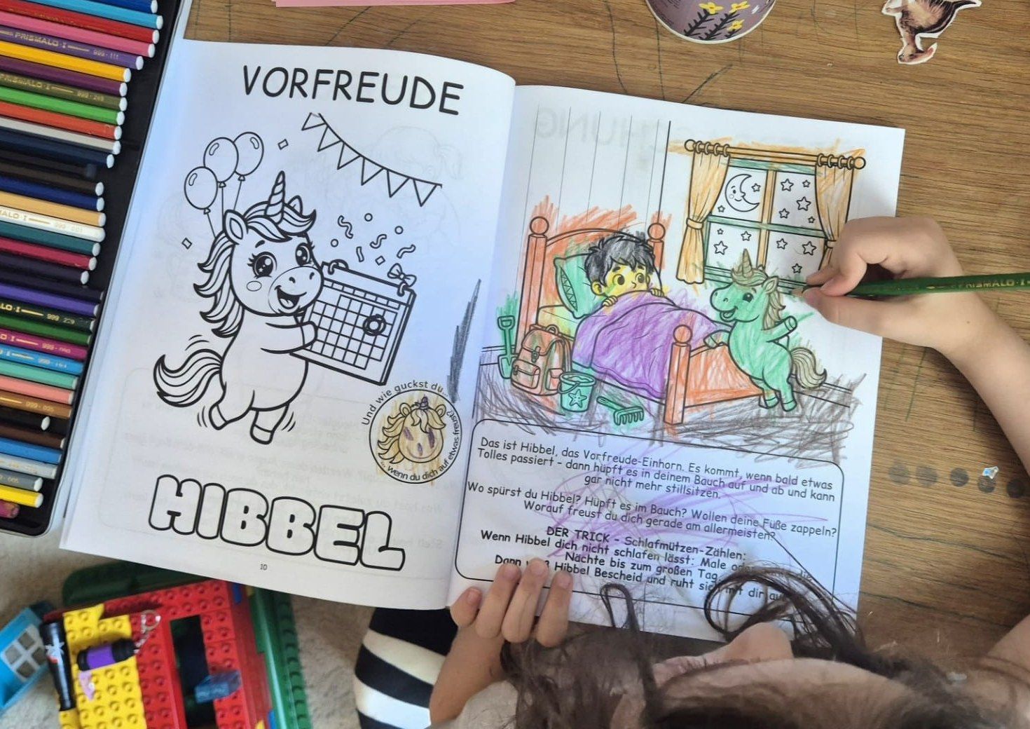 A child coloring the Excitement double page with colored pencils; on the left the unicorn Wiggles, on the right a scene with a child in bed.